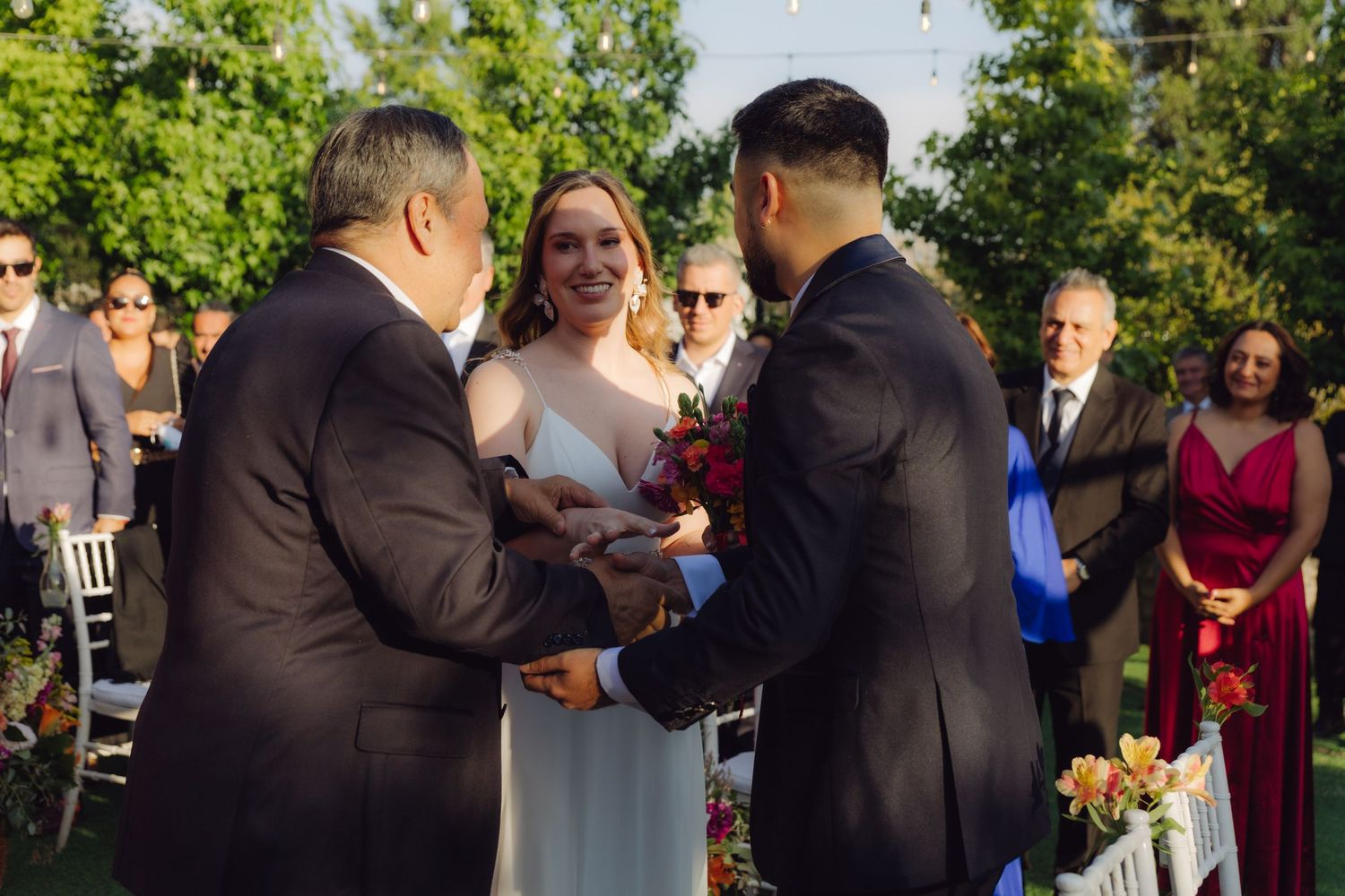 Father of the bride hands off daughter to groom at outdoor wedding ceremony altar.