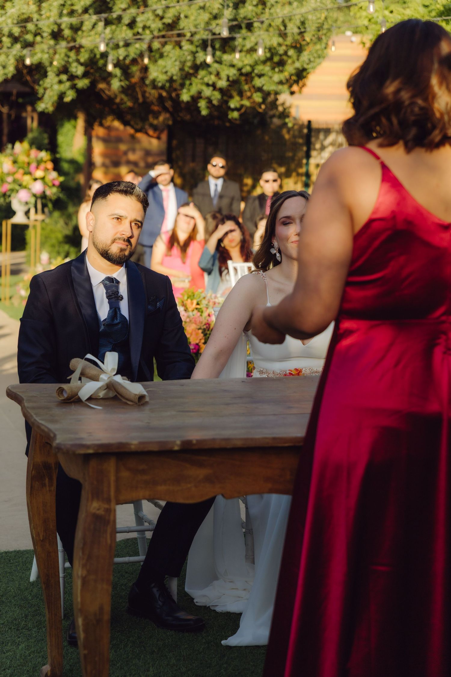 Groom listens attentively to officiant in red dress during intimate outdoor wedding ceremony.
