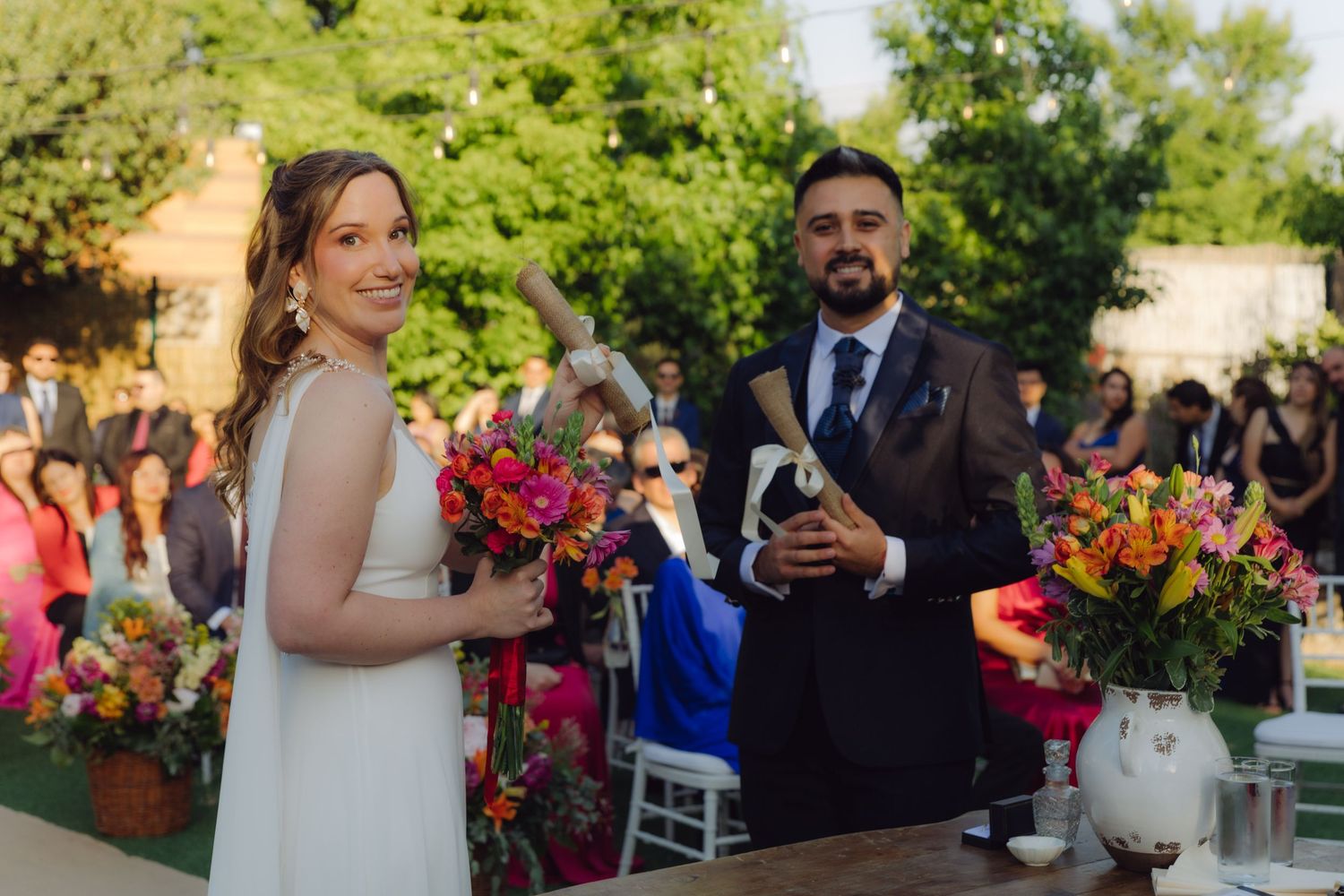 Smiling bride and groom standing together at outdoor wedding ceremony with vibrant floral decor.