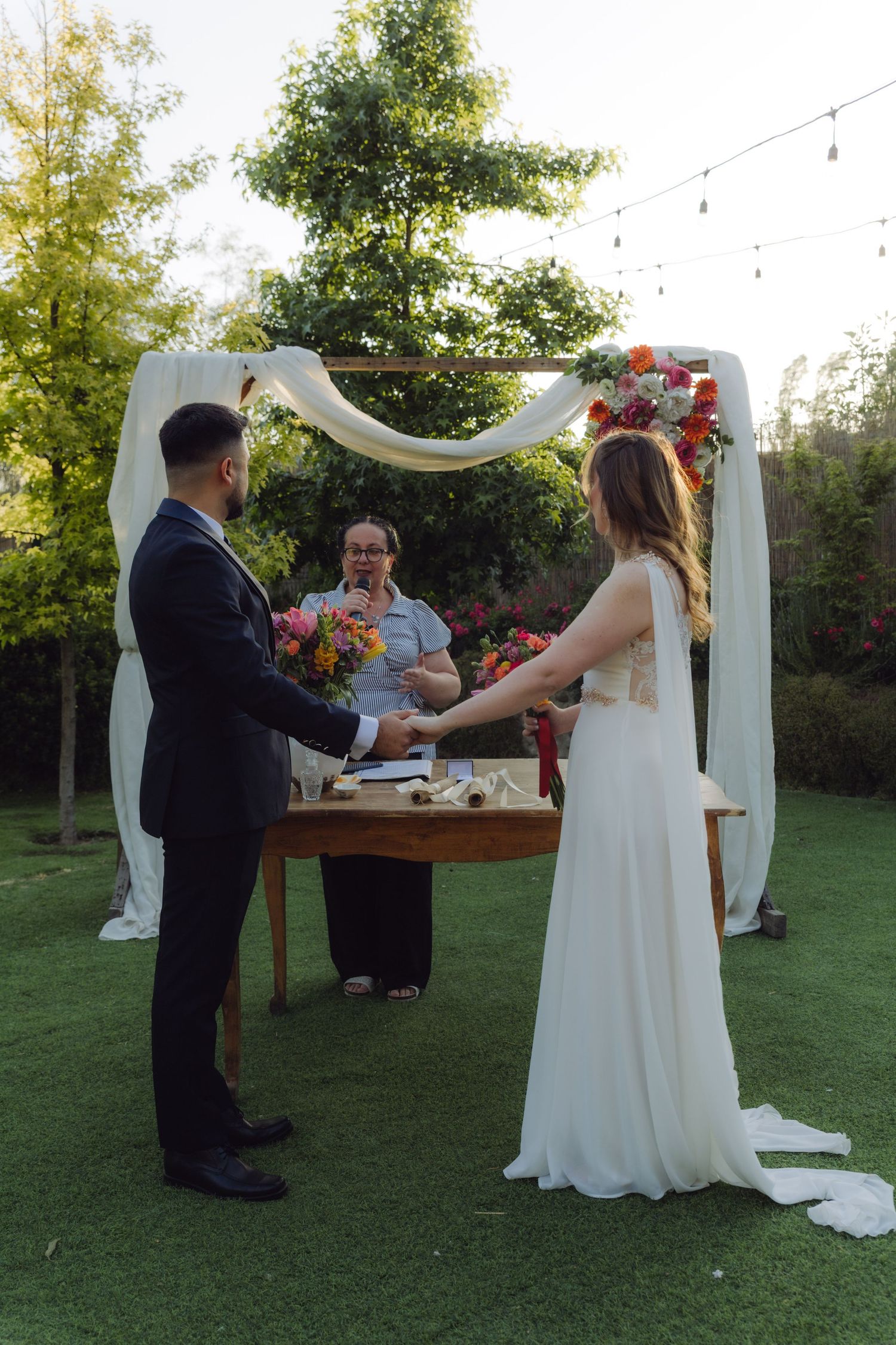Bride and groom exchanging vows under floral arch at outdoor garden wedding ceremony.
