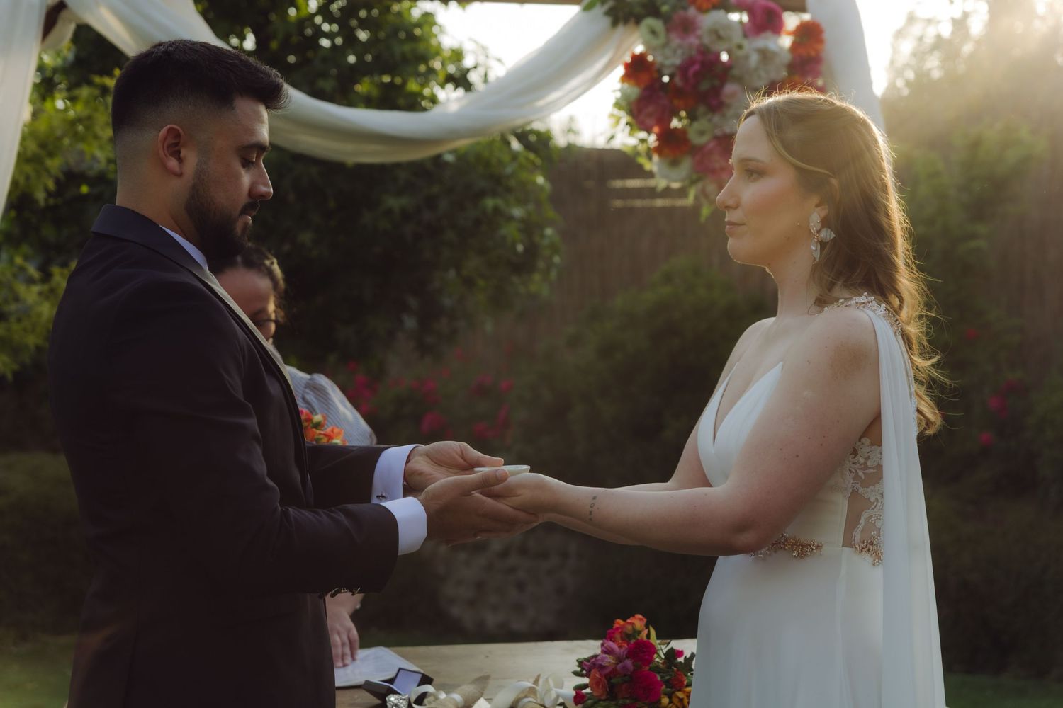 Couple holds hands at sunset during an intimate outdoor garden wedding ceremony.