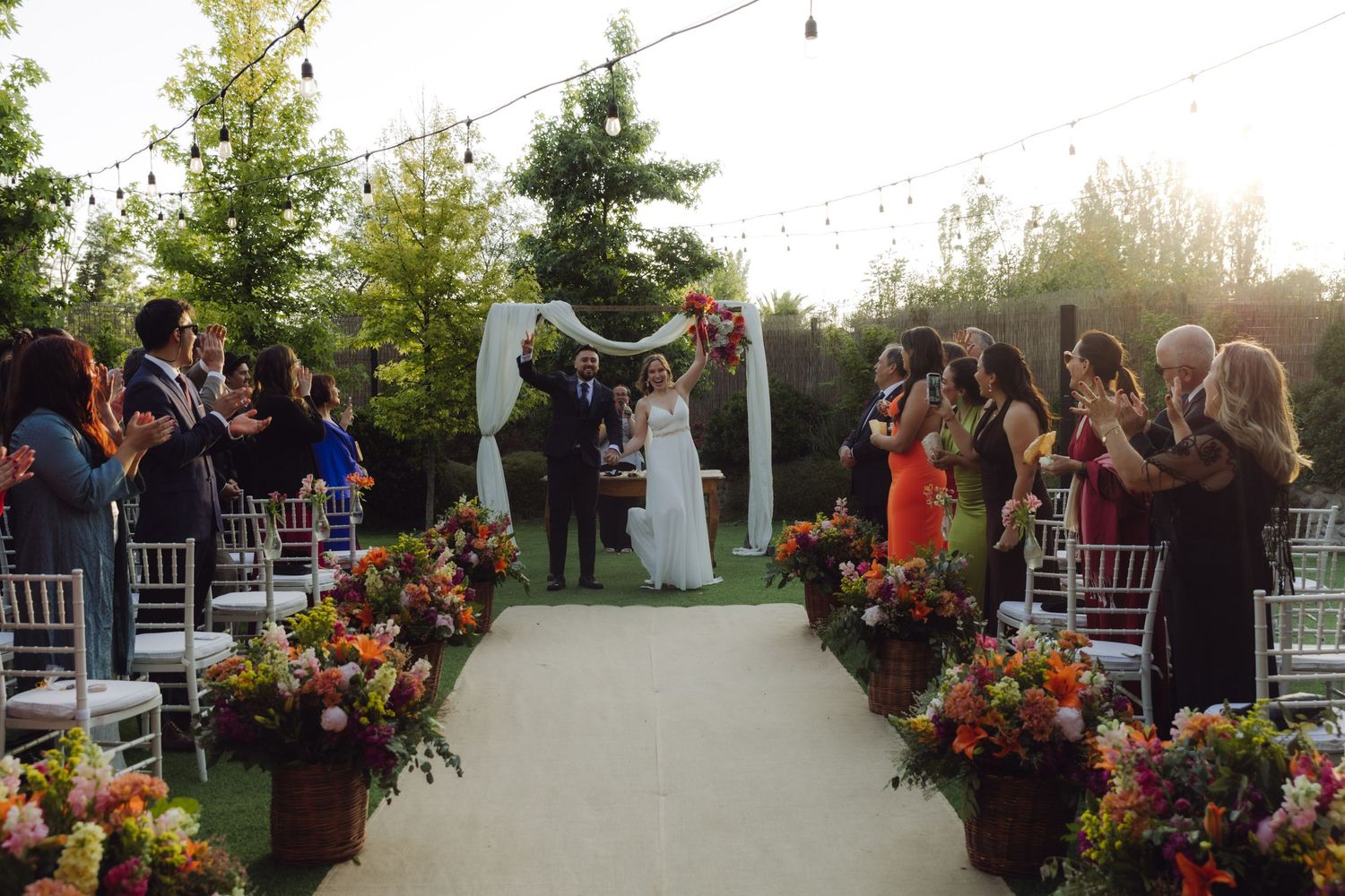 Couple walks down the aisle at a garden wedding surrounded by guests and colorful flowers.