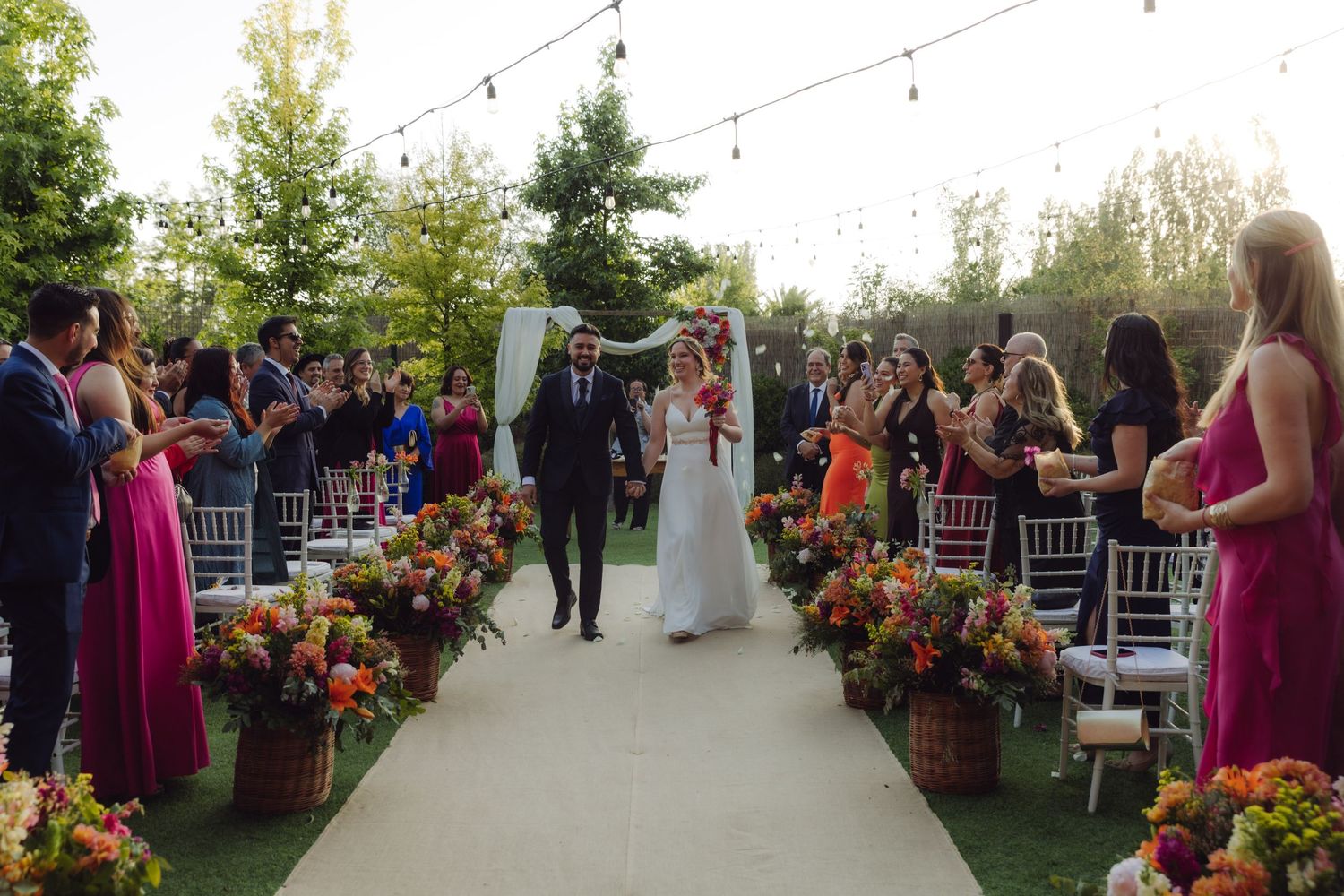 Newlyweds walk hand in hand down the aisle at an outdoor garden wedding ceremony.