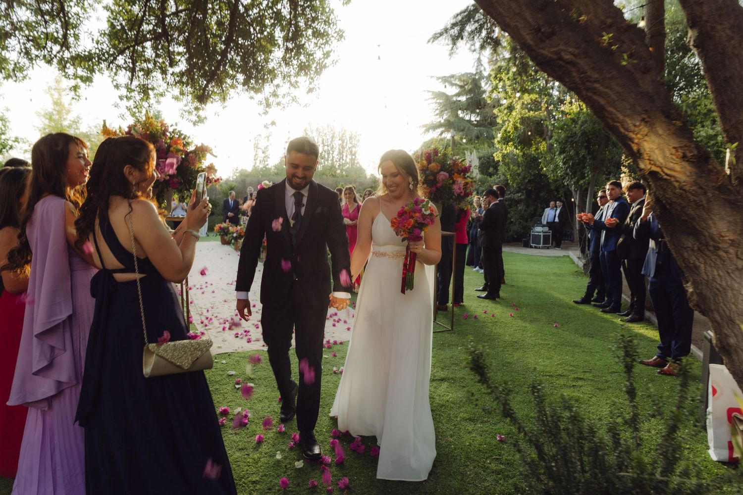 Bride and groom walk through a garden aisle as guests toss flower petals in celebration.