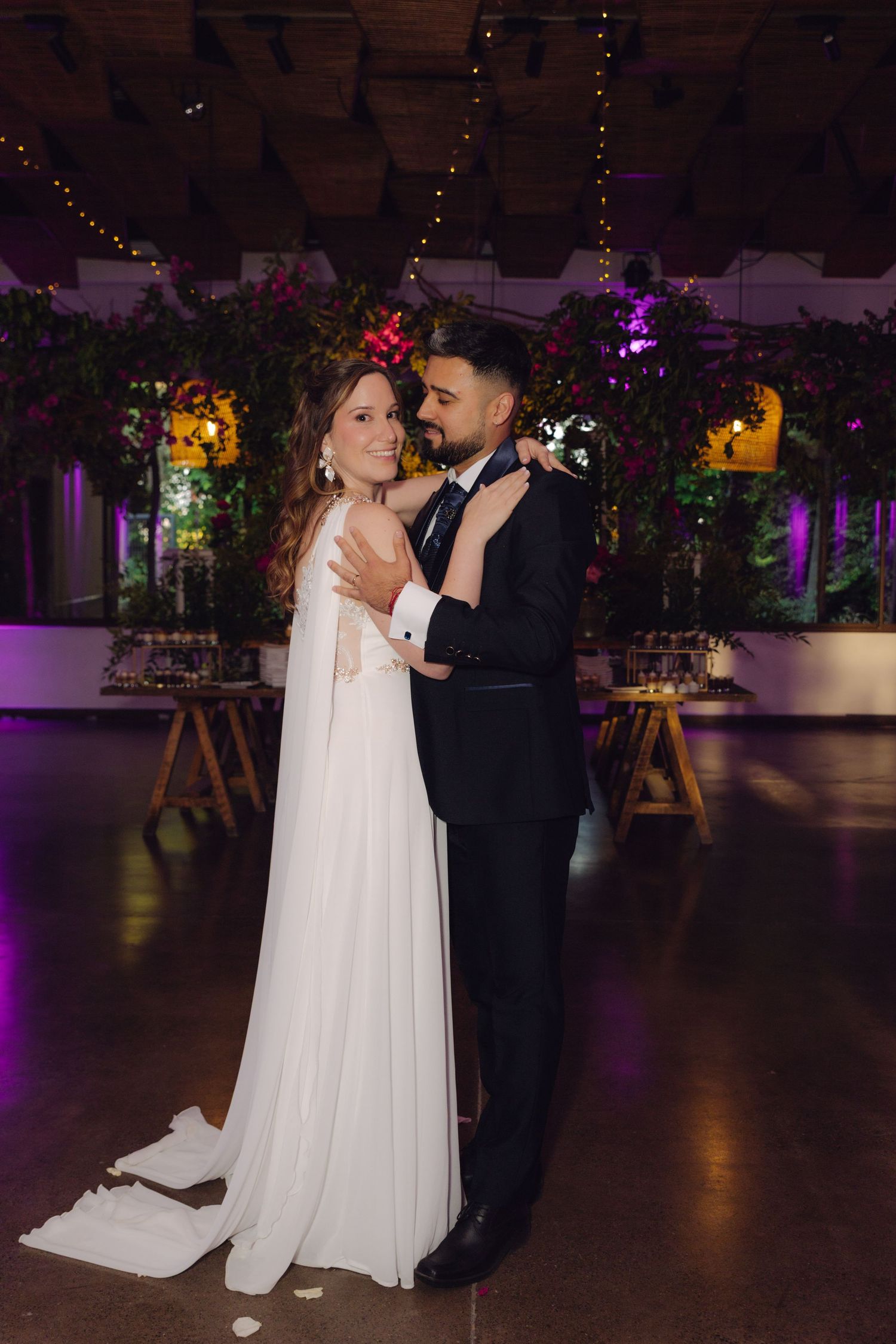Newlyweds embrace on the dance floor at a romantic indoor wedding reception with floral decor.