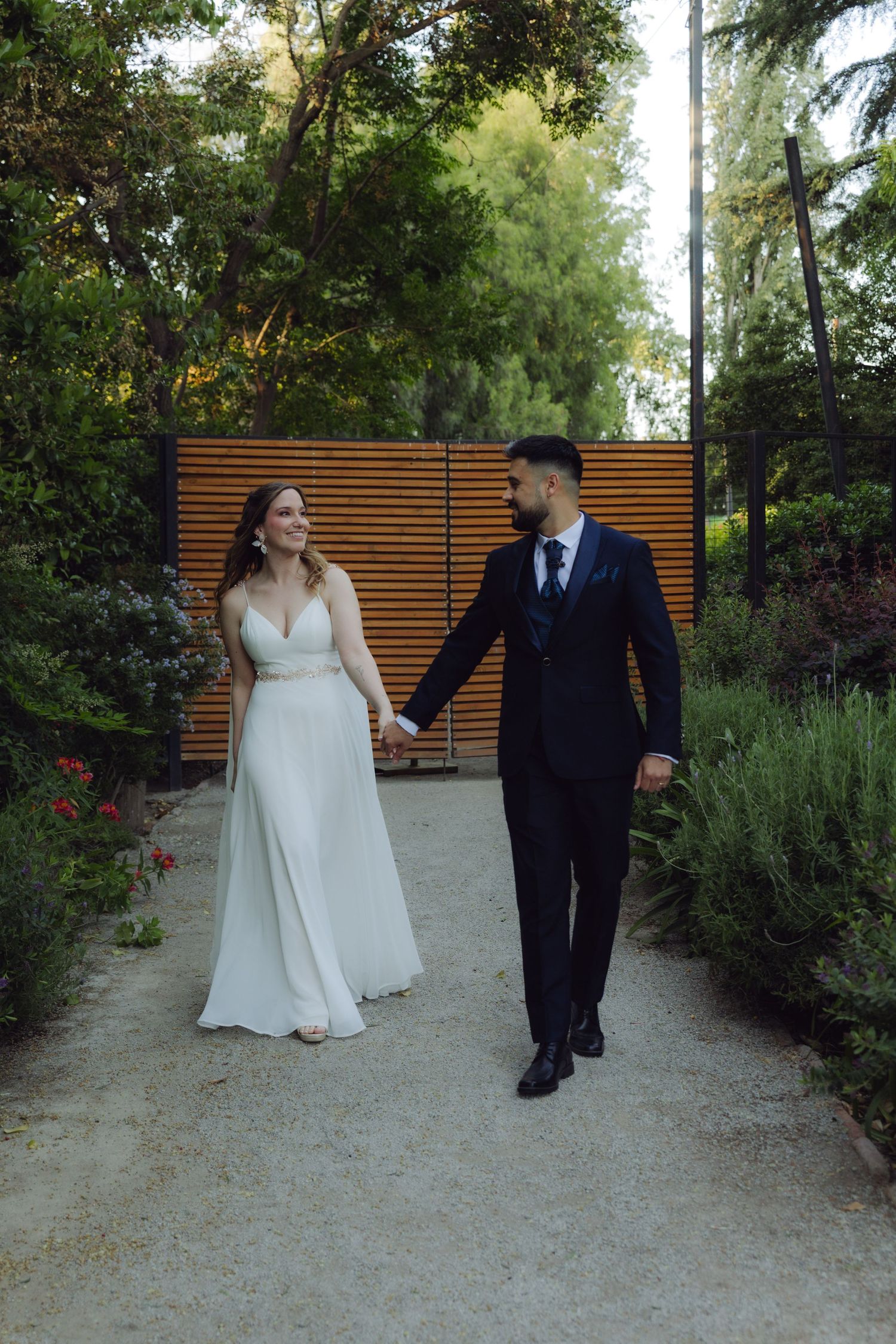 Bride and groom hold hands walking along a garden path on their wedding day.