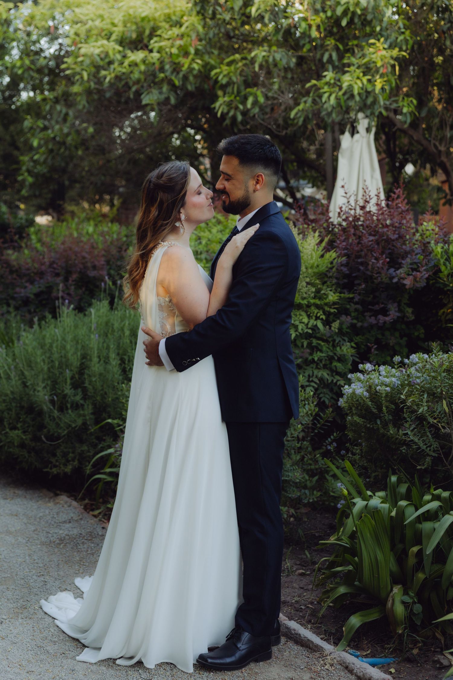 Bride and groom hold each other close smiling in a lush green garden.
