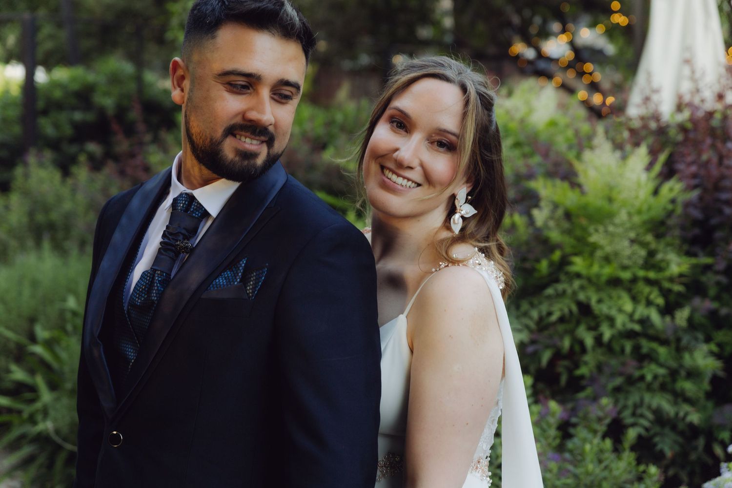 Bride and groom smile together in a lush garden setting on their wedding day.
