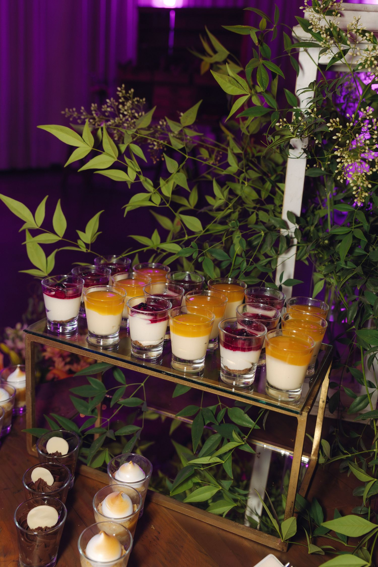 Gold tiered display stand with layered panna cotta dessert cups in purple-lit wedding reception setting.