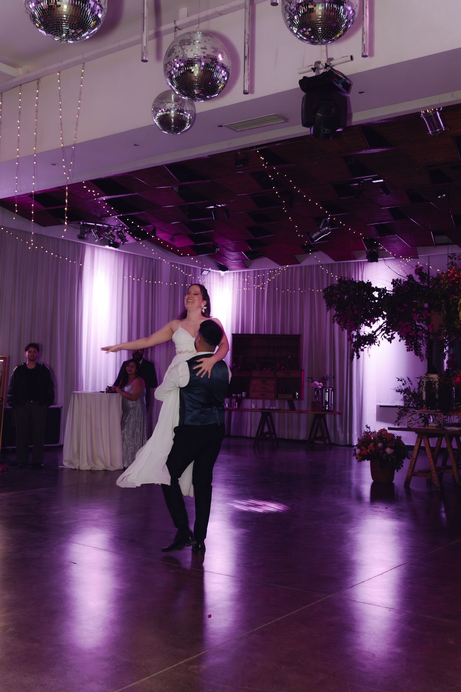 Bride and groom perform a choreographed first dance with a dramatic dip in a purple-lit wedding reception venue.