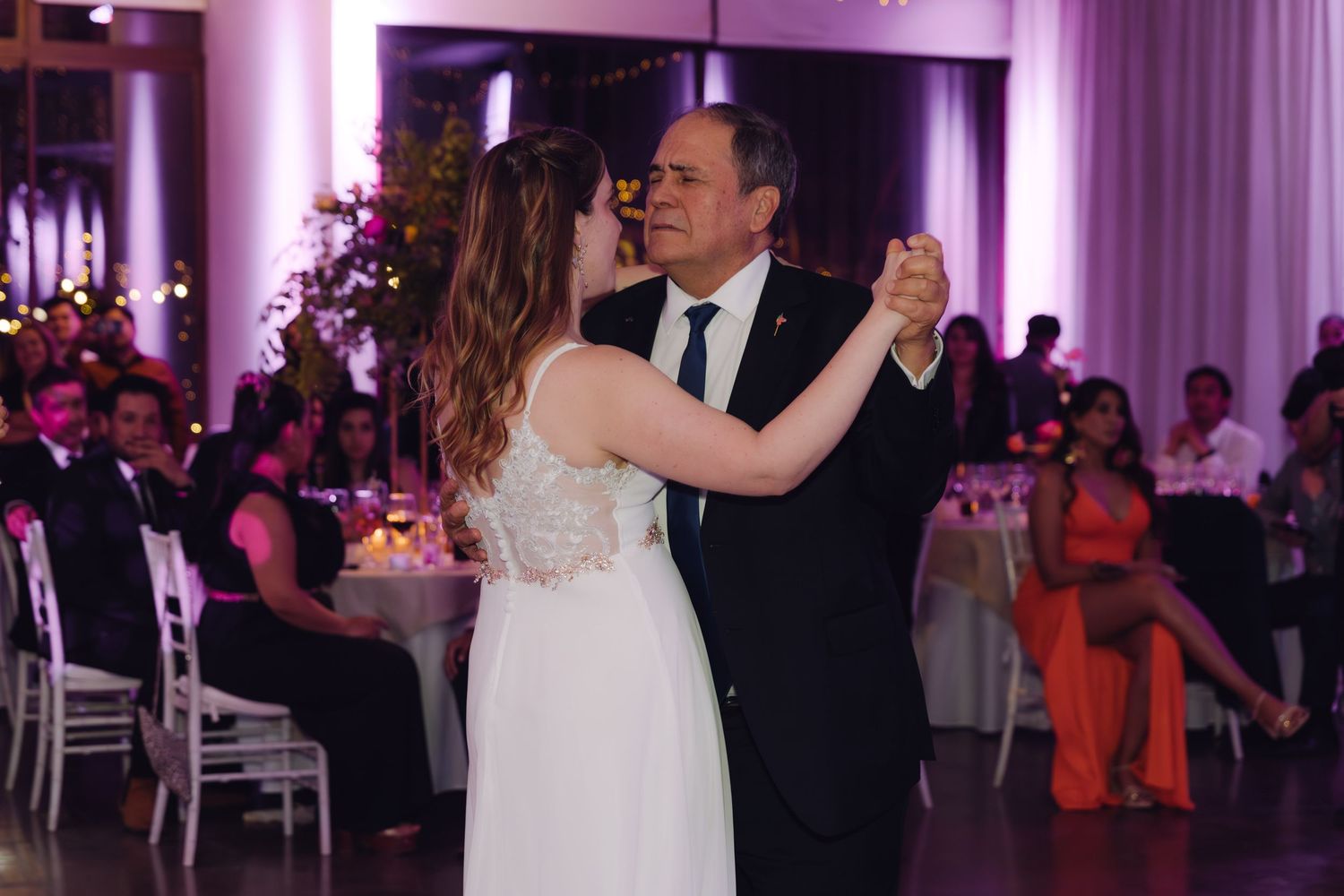 Bride shares a tender father-daughter dance in an elegant wedding reception hall with floral decorations.