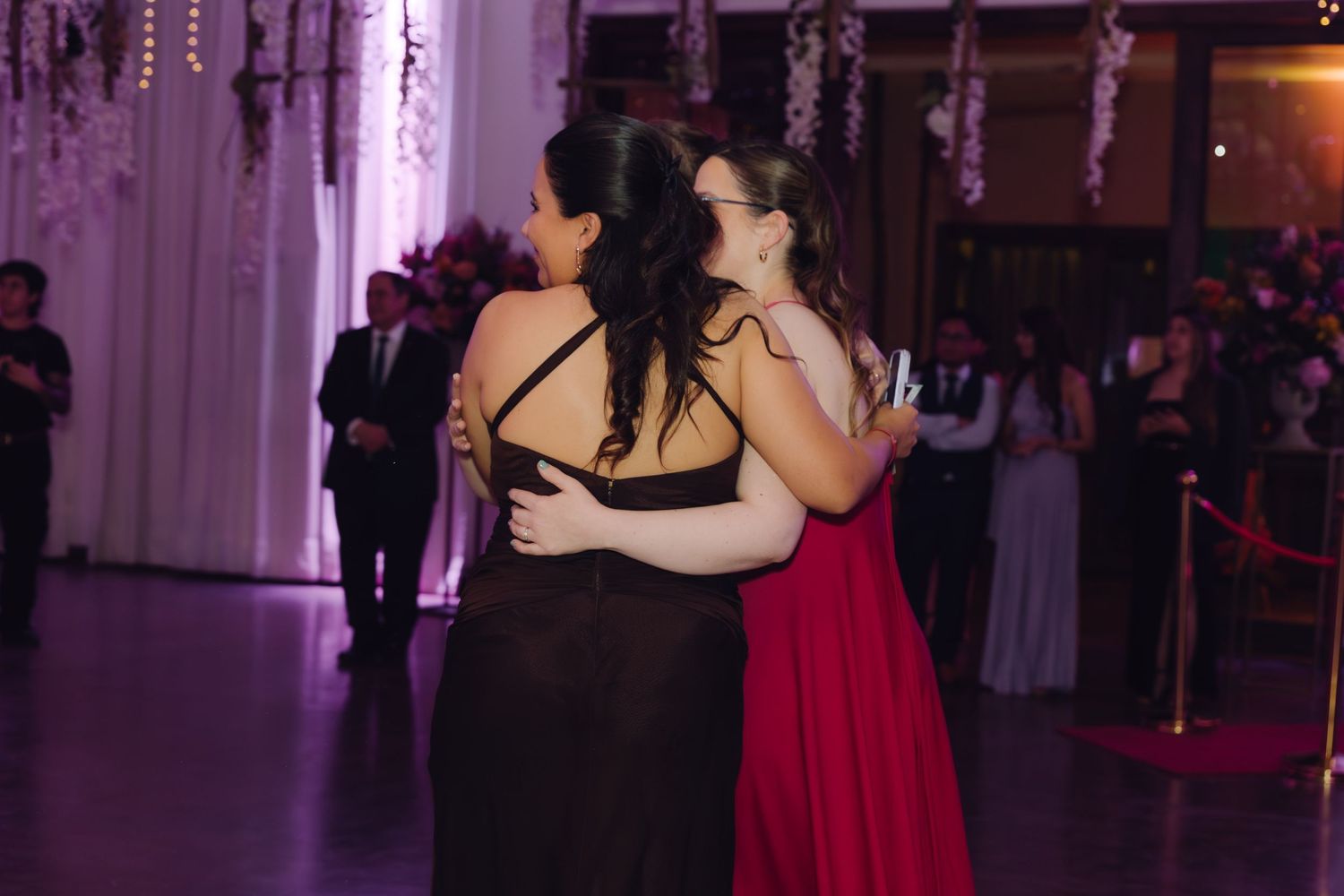 Two women in elegant gowns sharing a warm embrace on the wedding dance floor.