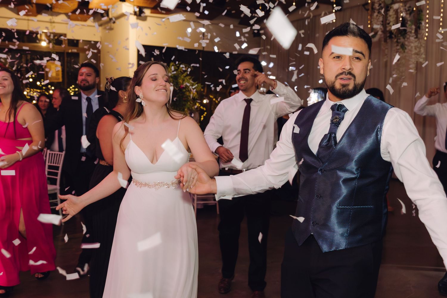 Bride and groom dancing joyfully amid falling confetti at their wedding reception.