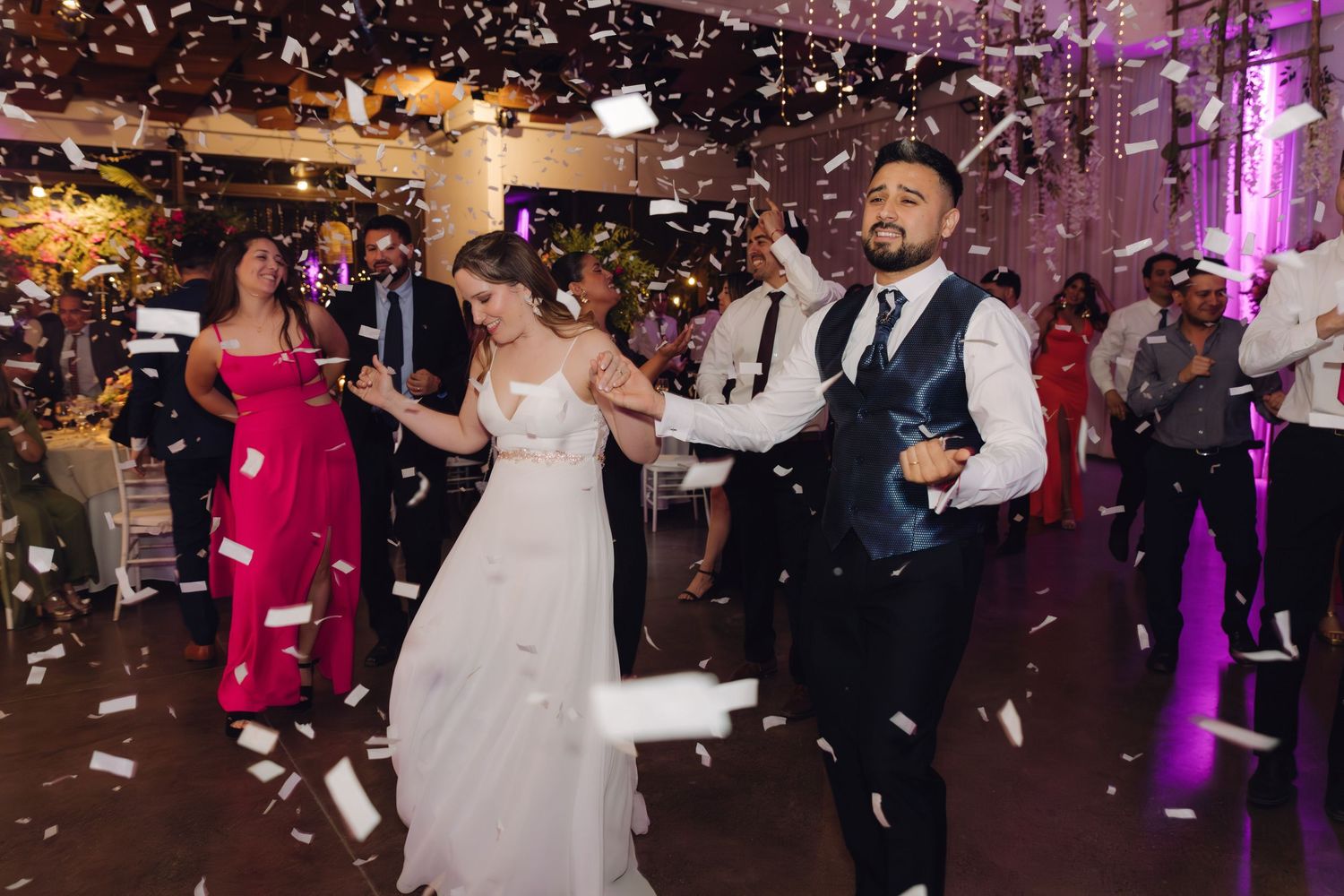Newlyweds share first dance surrounded by confetti and wedding guests in elegant venue.