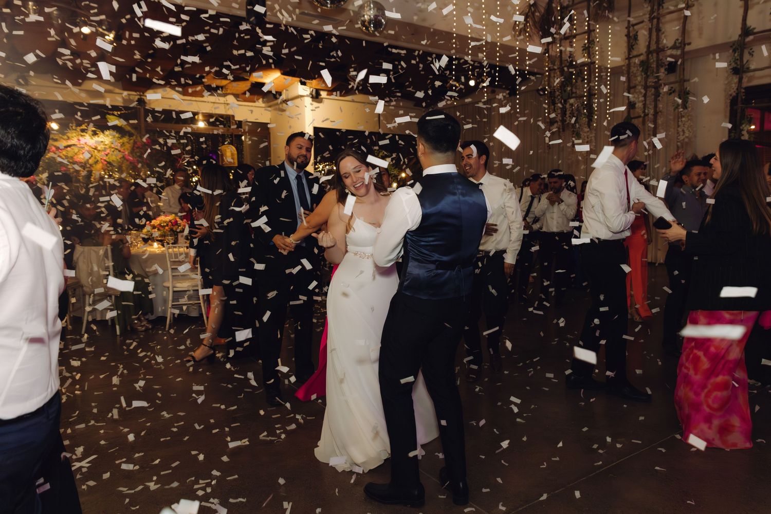 Newlyweds share first dance in a shower of white confetti at their wedding celebration.