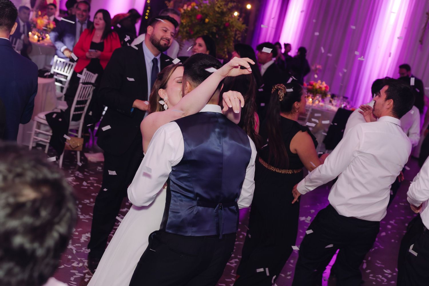 Bride and groom dance together surrounded by celebrating guests at wedding reception.