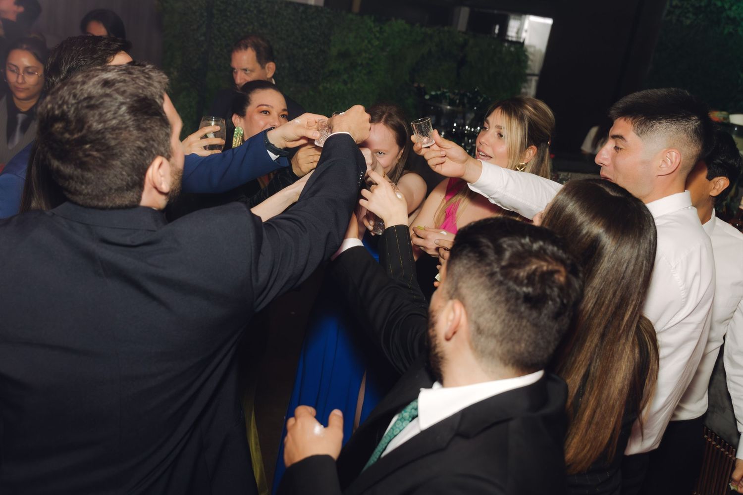 Excited wedding guests raise champagne glasses together in a celebratory group toast.