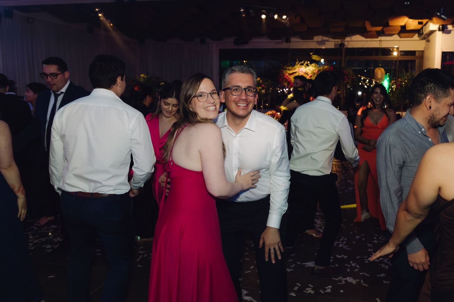 Smiling couple in red and white embracing on the dance floor at a wedding reception.