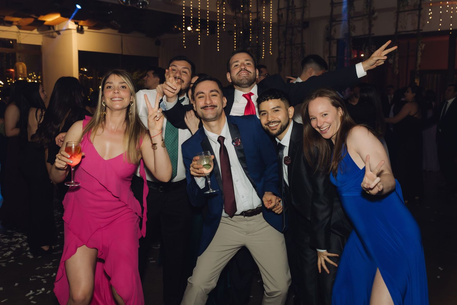 Group of friends posing and dancing at a formal wedding reception party.
