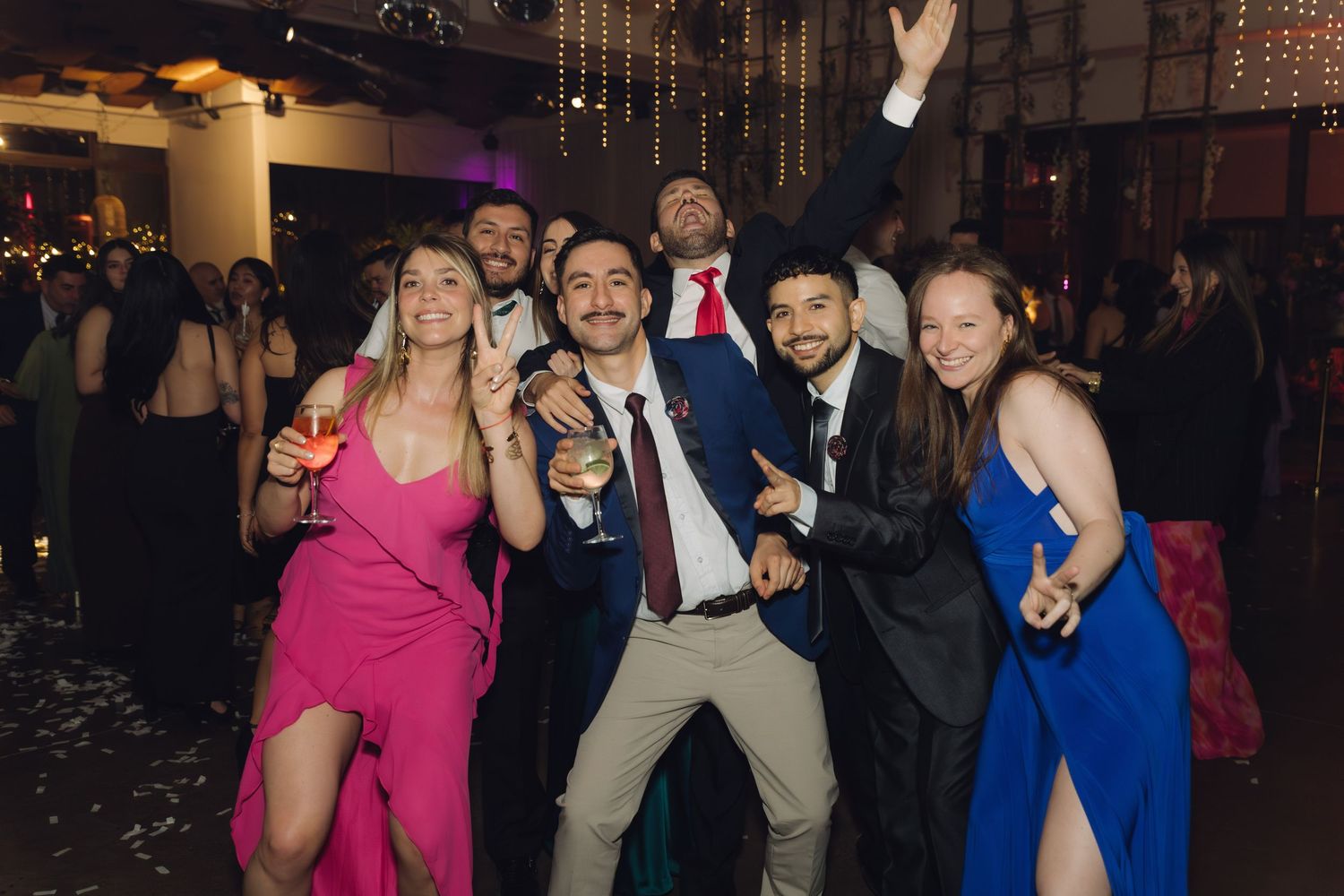 Friends in formal attire dancing and posing joyfully at a wedding party.