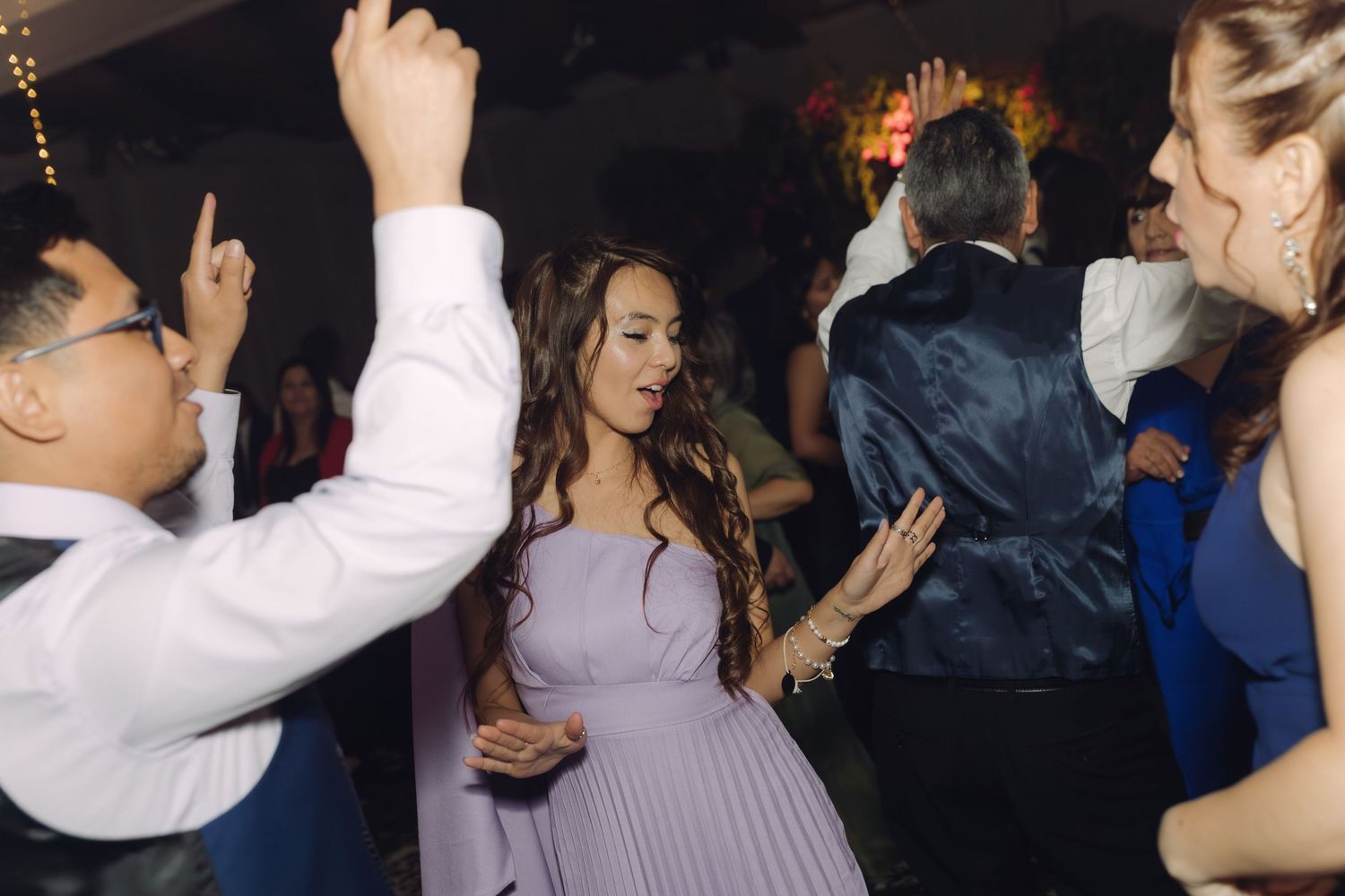 Woman in lavender dress dancing at a lively wedding reception celebration.