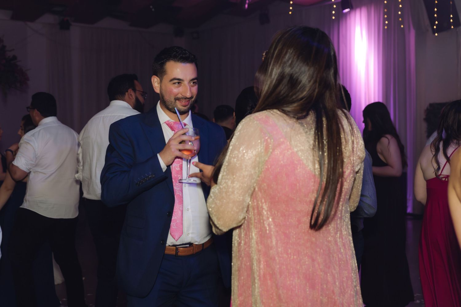 Man in blue suit smiling while dancing with a woman at a wedding.