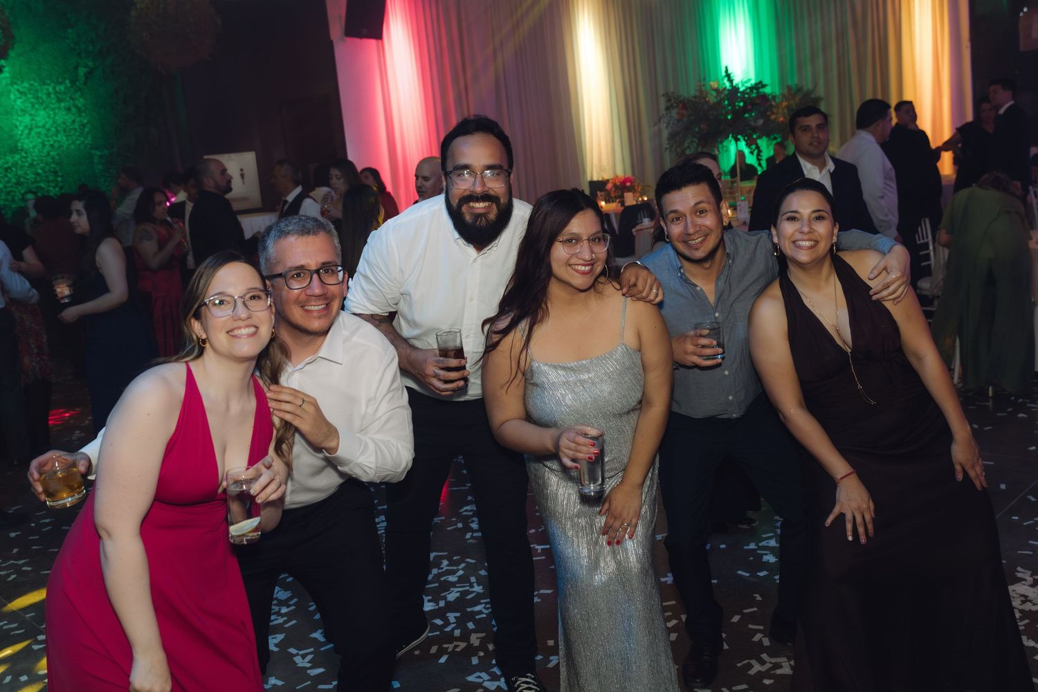 Group of six wedding guests posing and smiling together on dance floor at festive reception.