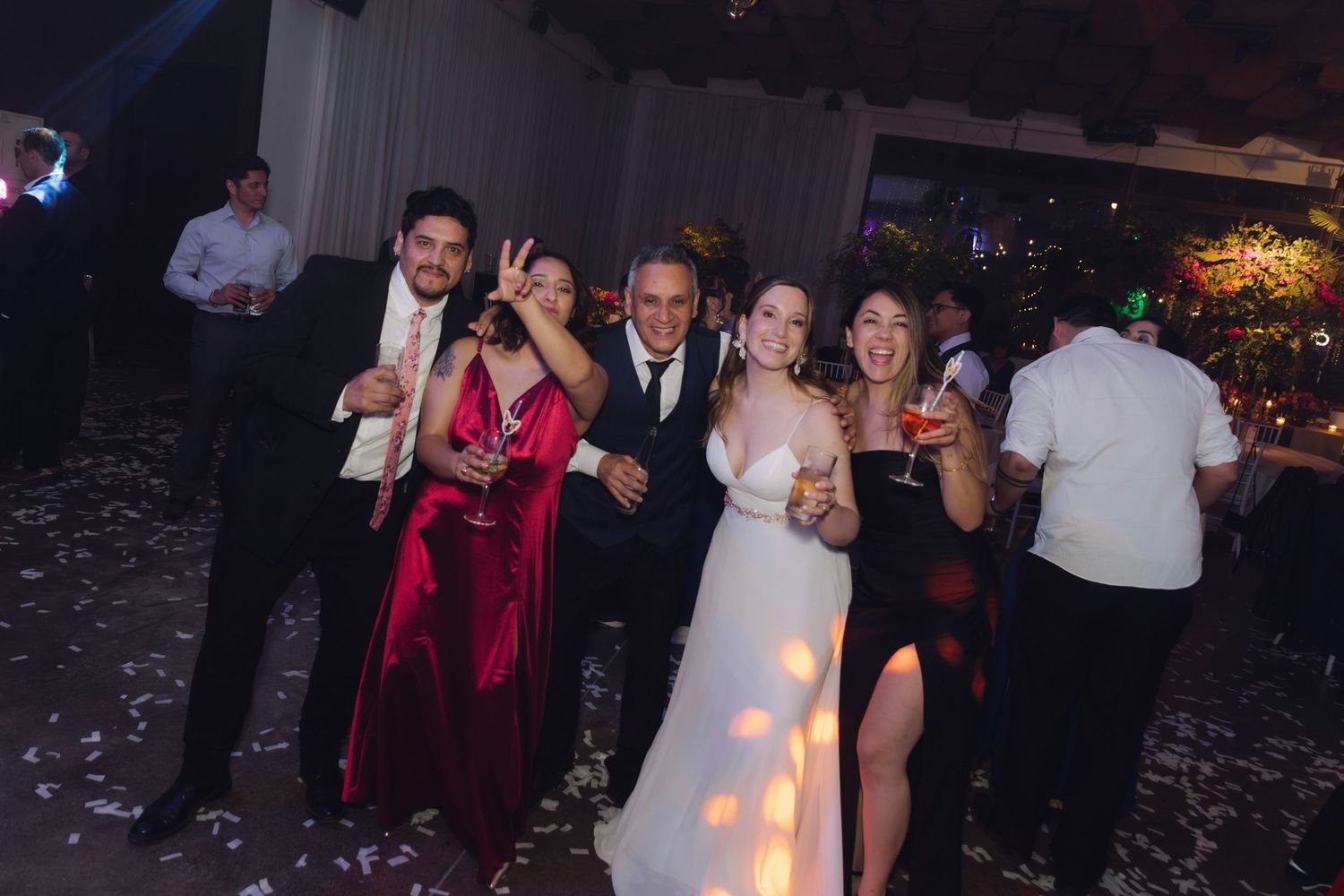 Wedding party guests celebrate with drinks on confetti-filled dance floor at elegant reception.