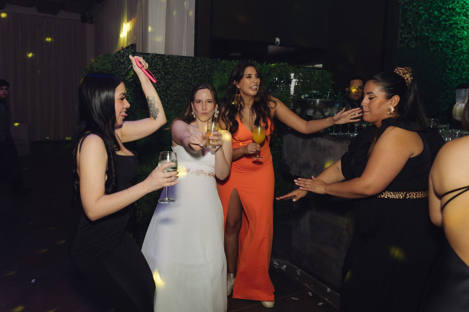Bride in white dress dances with friends in colorful gowns at lively wedding reception.