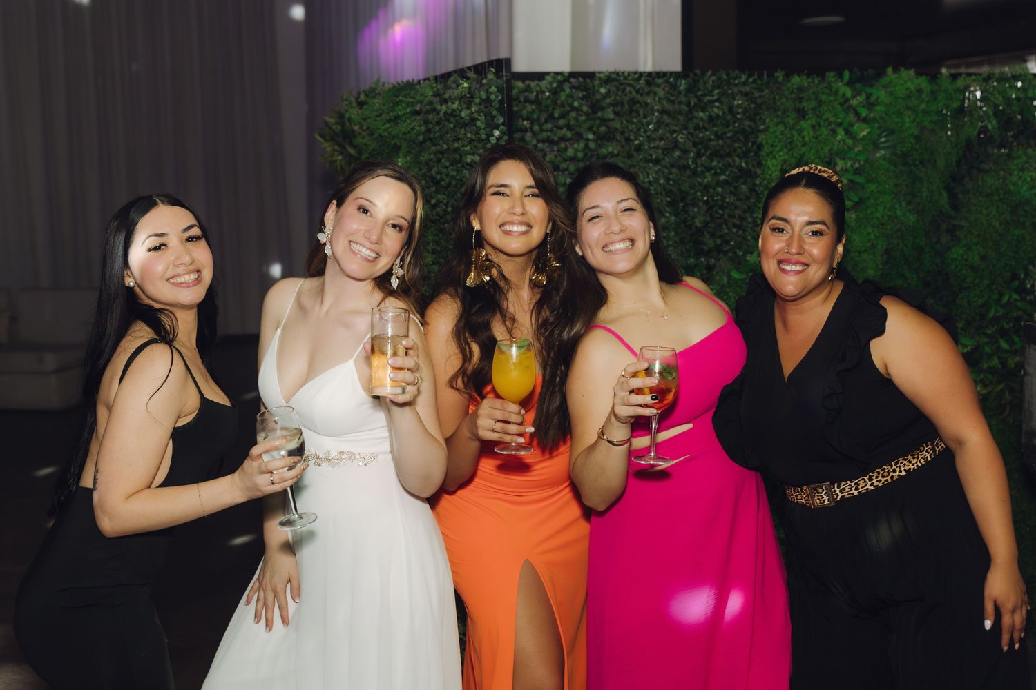 Bride and four bridesmaids in colorful dresses pose with drinks at wedding reception.
