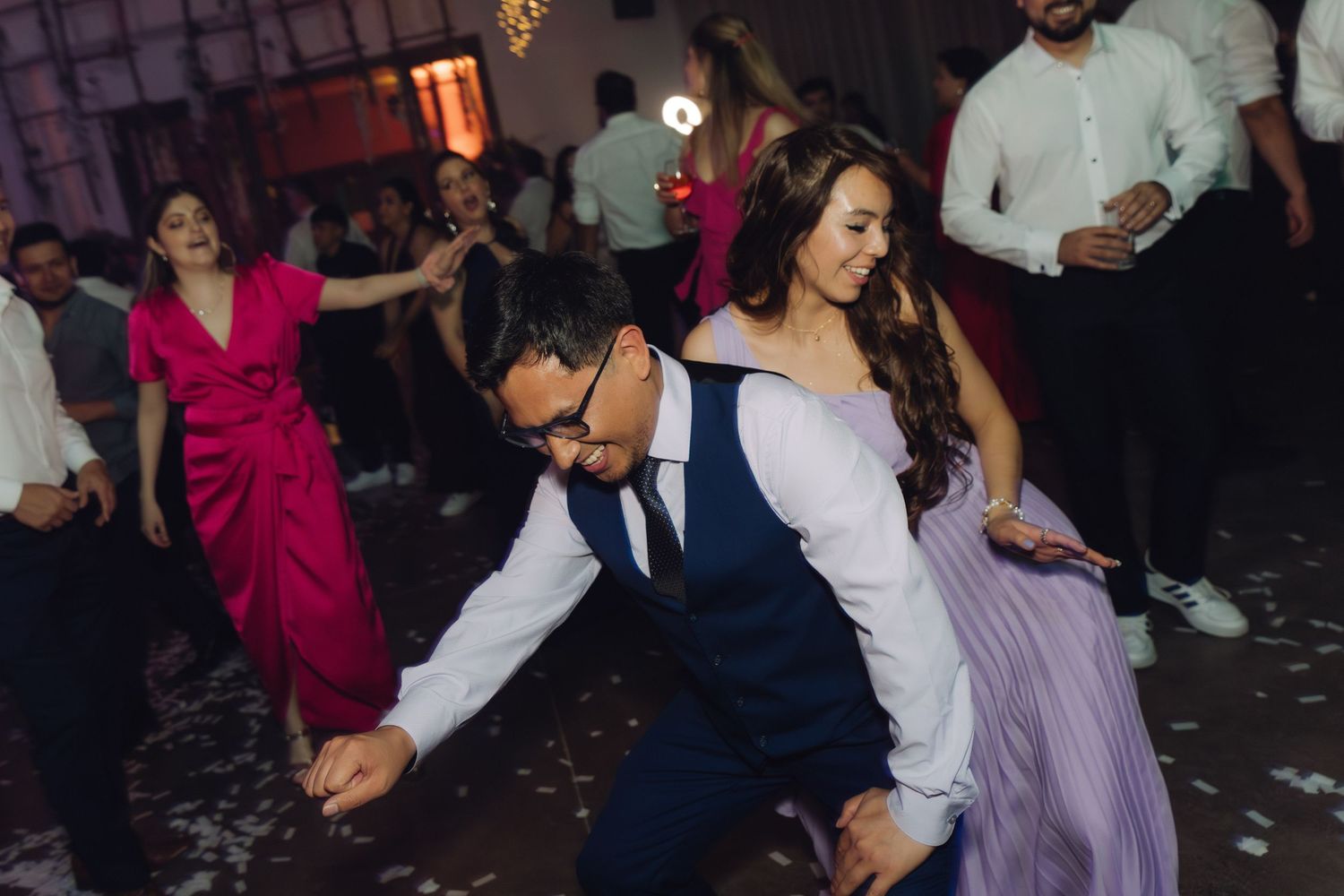 Couple dancing energetically at a wedding reception with guests celebrating in the background.
