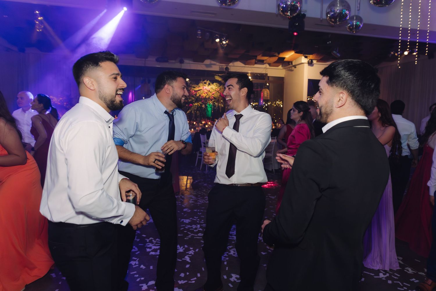 Four men in formal attire socializing and dancing at a festive wedding reception.