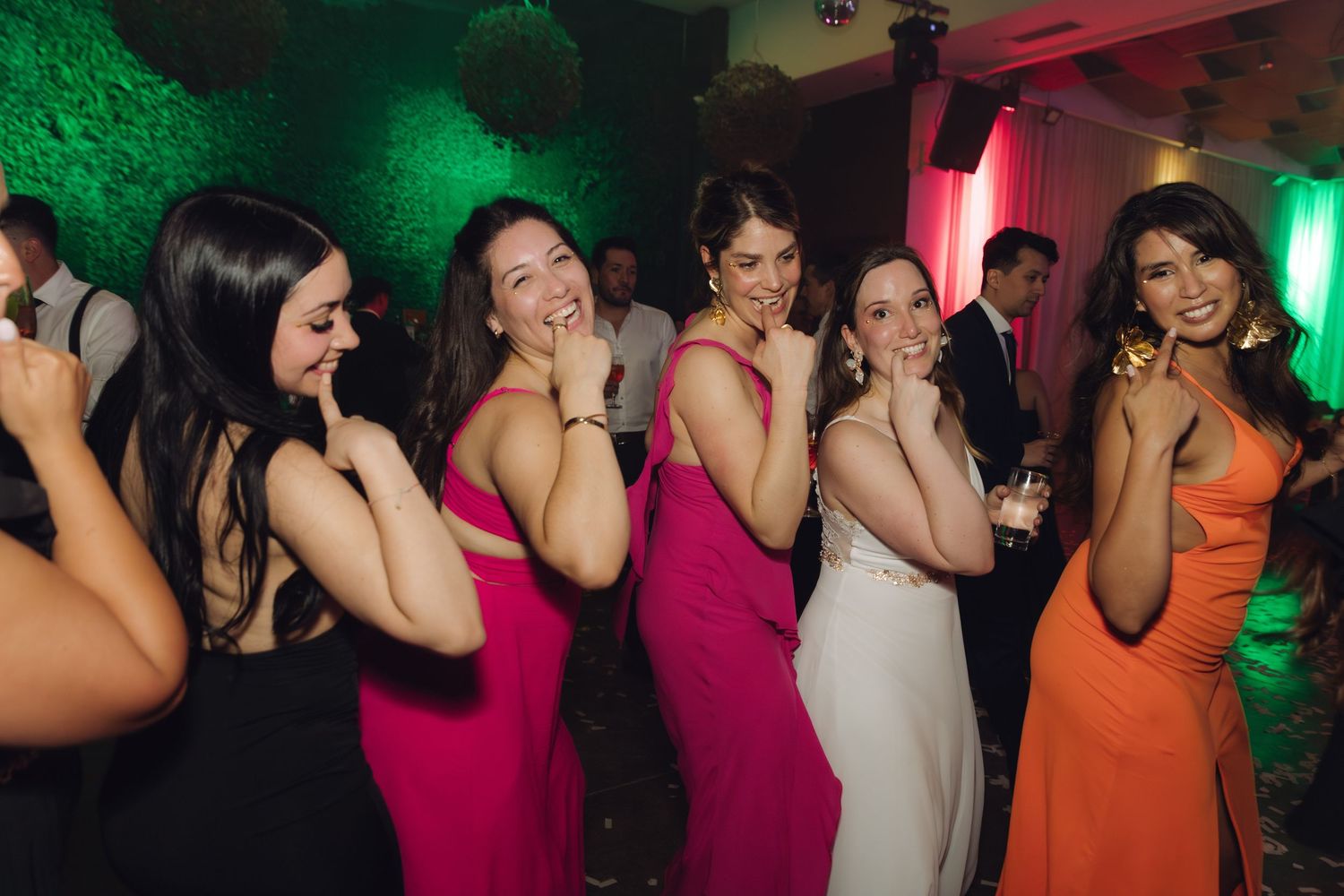 Bridesmaids in pink and orange dresses pose playfully with the bride at a wedding reception.