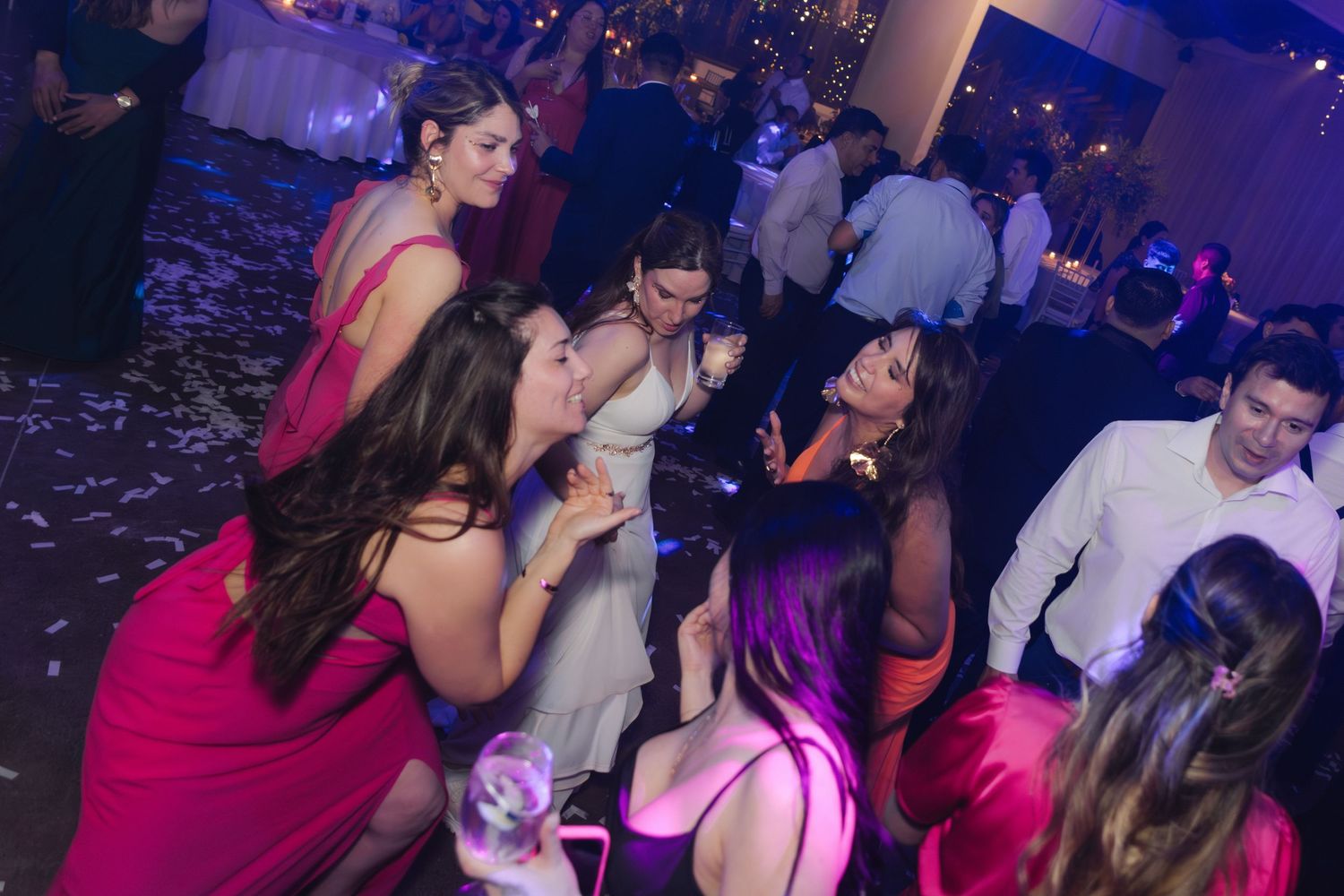 Guests in elegant dresses dance and celebrate energetically on a wedding reception dance floor.
