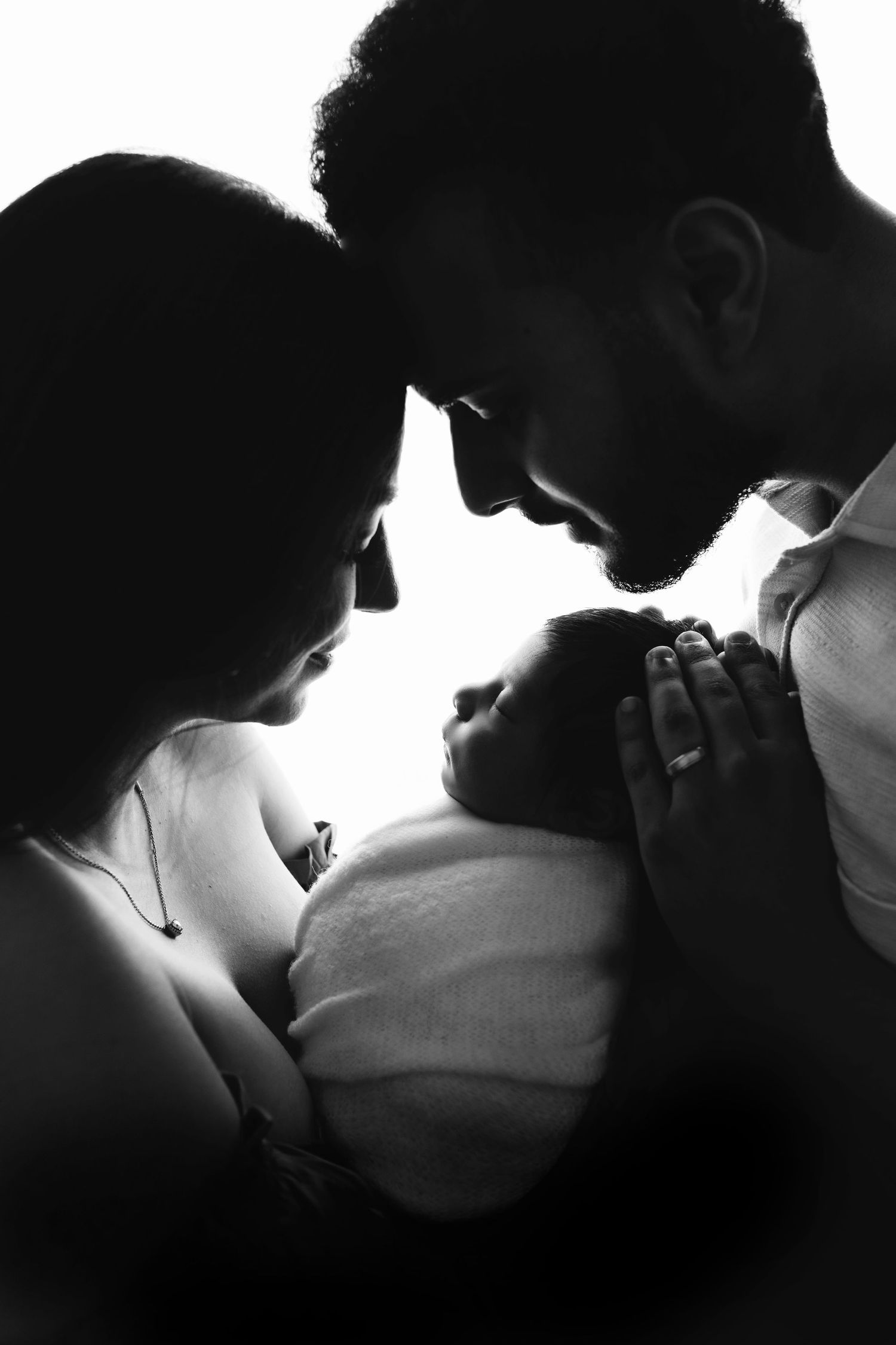 Black and white silhouette of parents tenderly cradling their newborn baby, a touching family portrait.