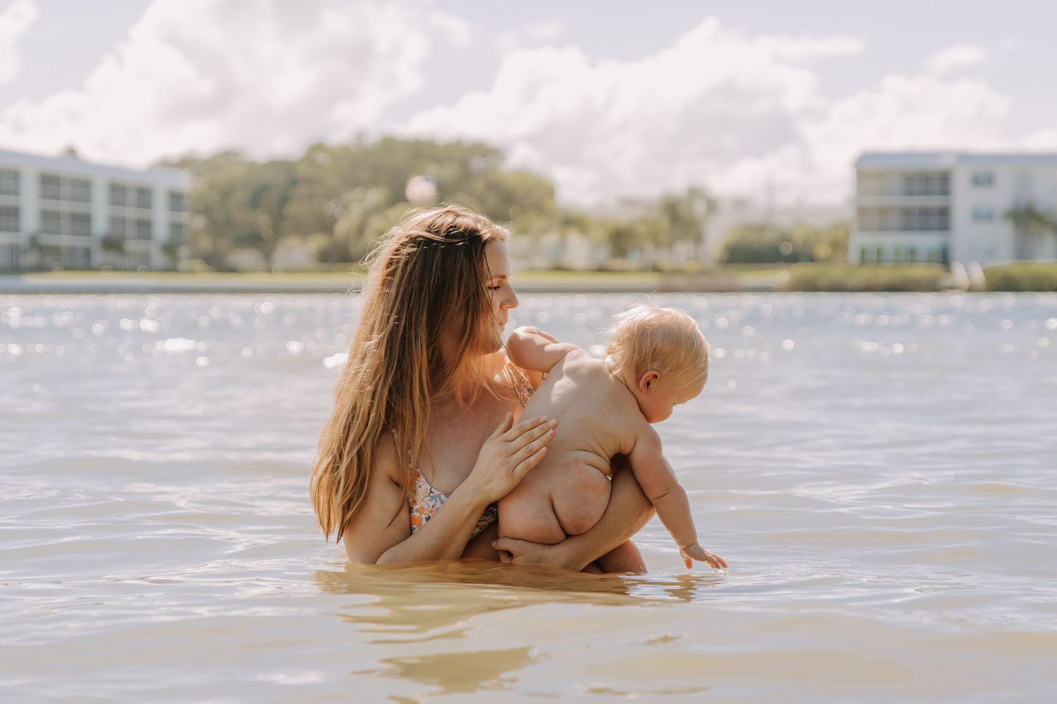 Mother holding baby in shallow water near beach resort on sunny day in jupiter inlet.