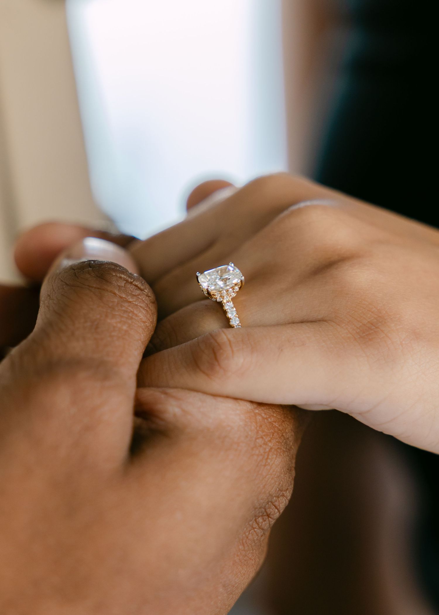 Close-up of a diamond engagement ring on a woman's finger as a man holds her hand tenderly.