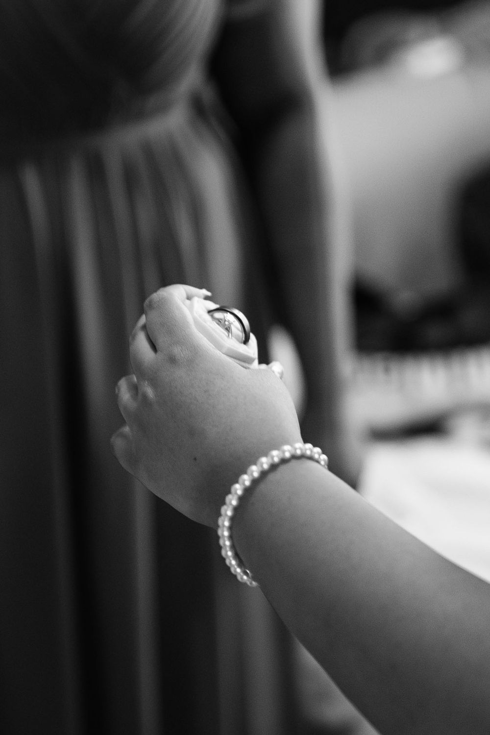 Black and white photo of a hand wearing a pearl bracelet holding wedding rings at a bridal ceremony.
