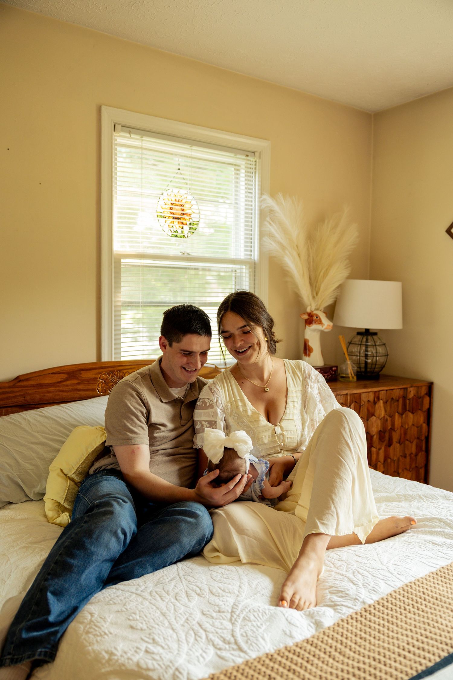 Young couple sitting on a bed smiling at their newborn baby in a cozy bedroom.