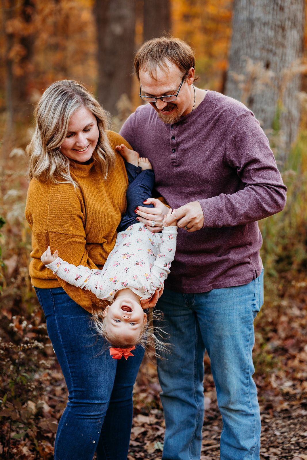 A mom and dad holding their little girl upside down playing. They are all smiling and laughing.