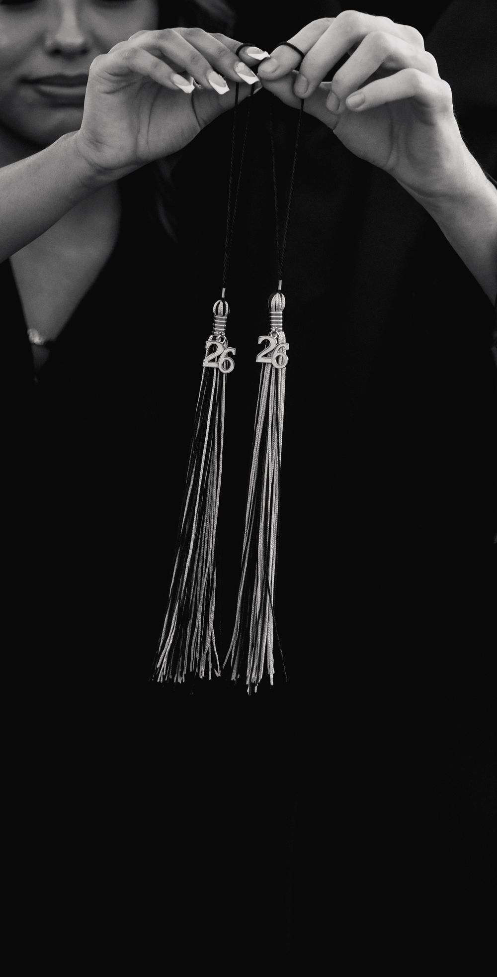 Black and white photo of hands holding two graduation tassels with 26 and 28 year charms.
