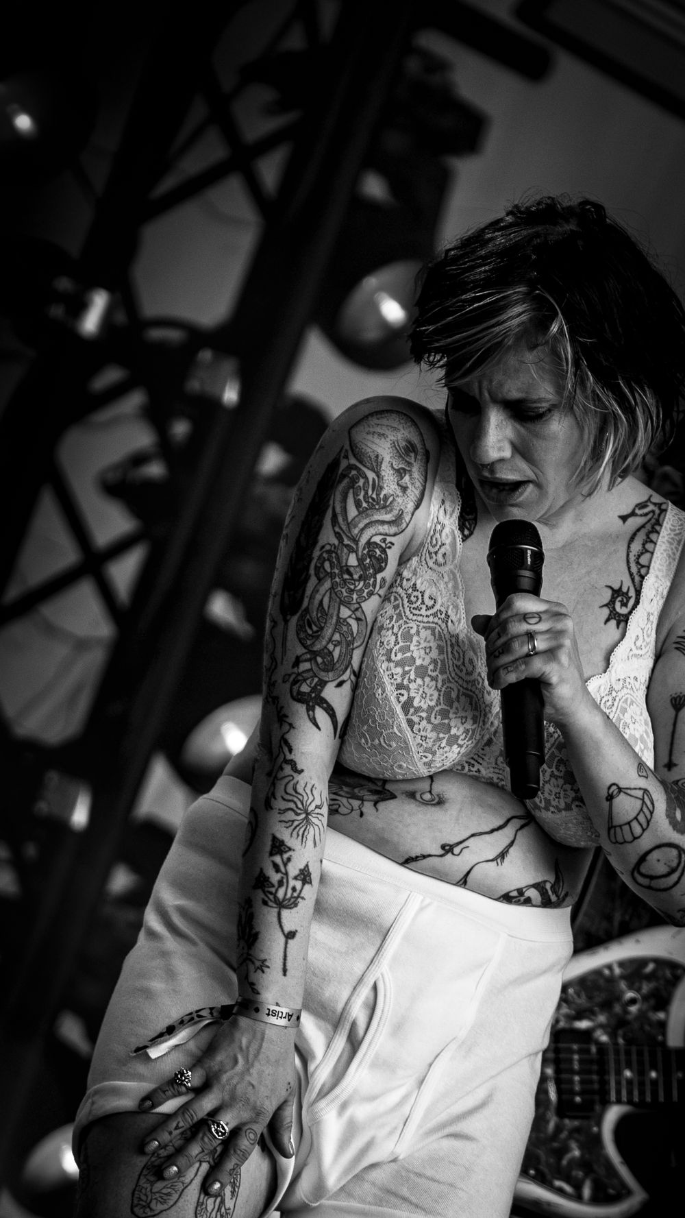Black and white photo of a heavily tattooed singer performing on stage holding a microphone.