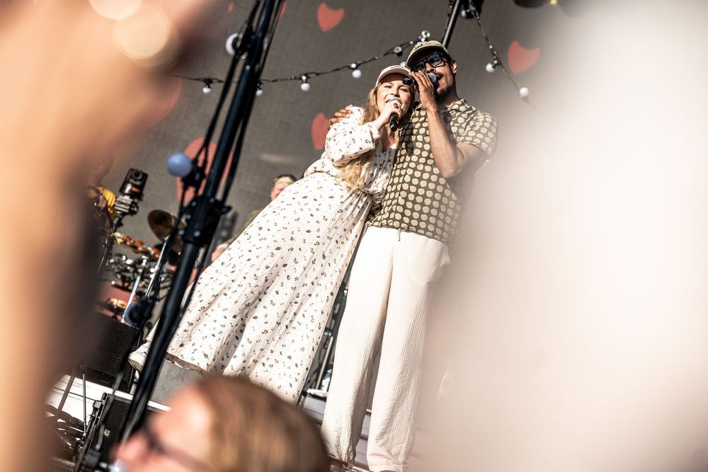 Two singers perform on stage under heart decorations, sharing a microphone at an intimate live music concert.
