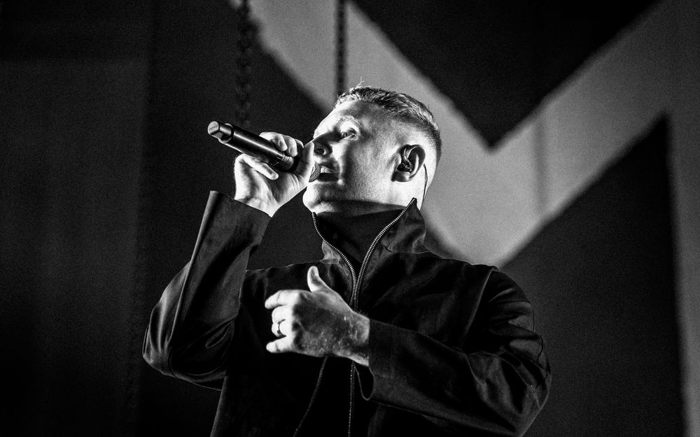 Black and white photo of a male singer performing on stage, holding a microphone with dramatic lighting.