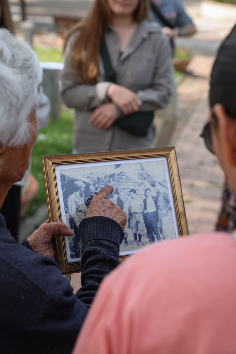 Elderly person holding a framed vintage black and white group photo outdoors.