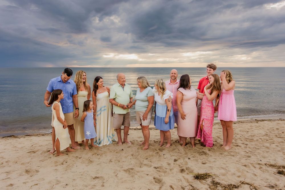 Extended family group candid photo on beach at sunset with overcast sky and ocean in background.