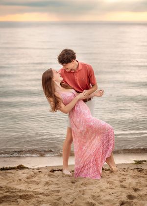 A young couple shares a romantic moment dancing closely together on a sandy beach at sunset.
