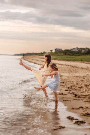 Two young girls laugh and splash in the ocean waves together on a sandy beach at sunset.