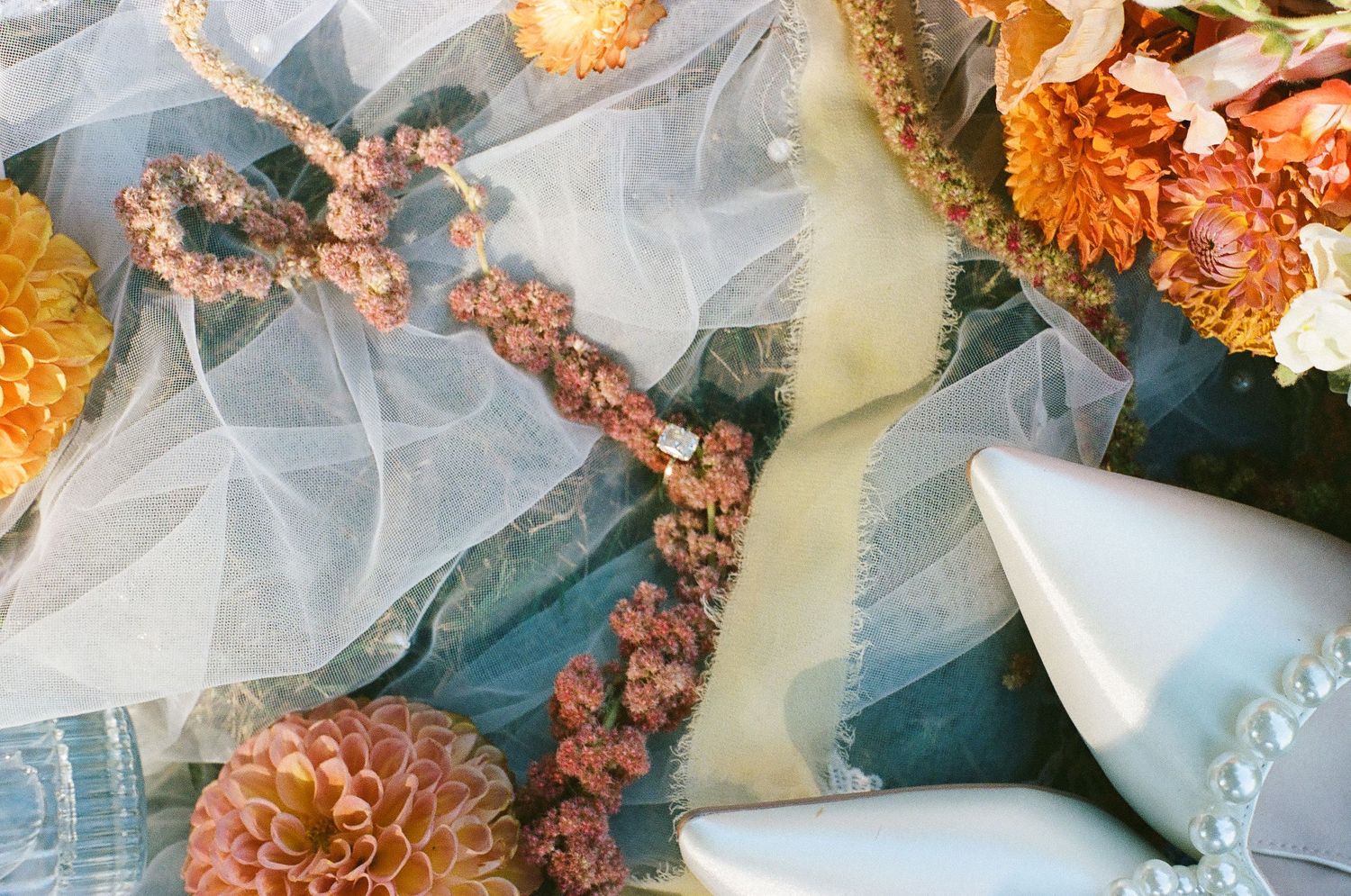 Autumn floral arrangement with orange dahlias, dried flowers, teal fabric, pearl beads, and a white ceramic piece.