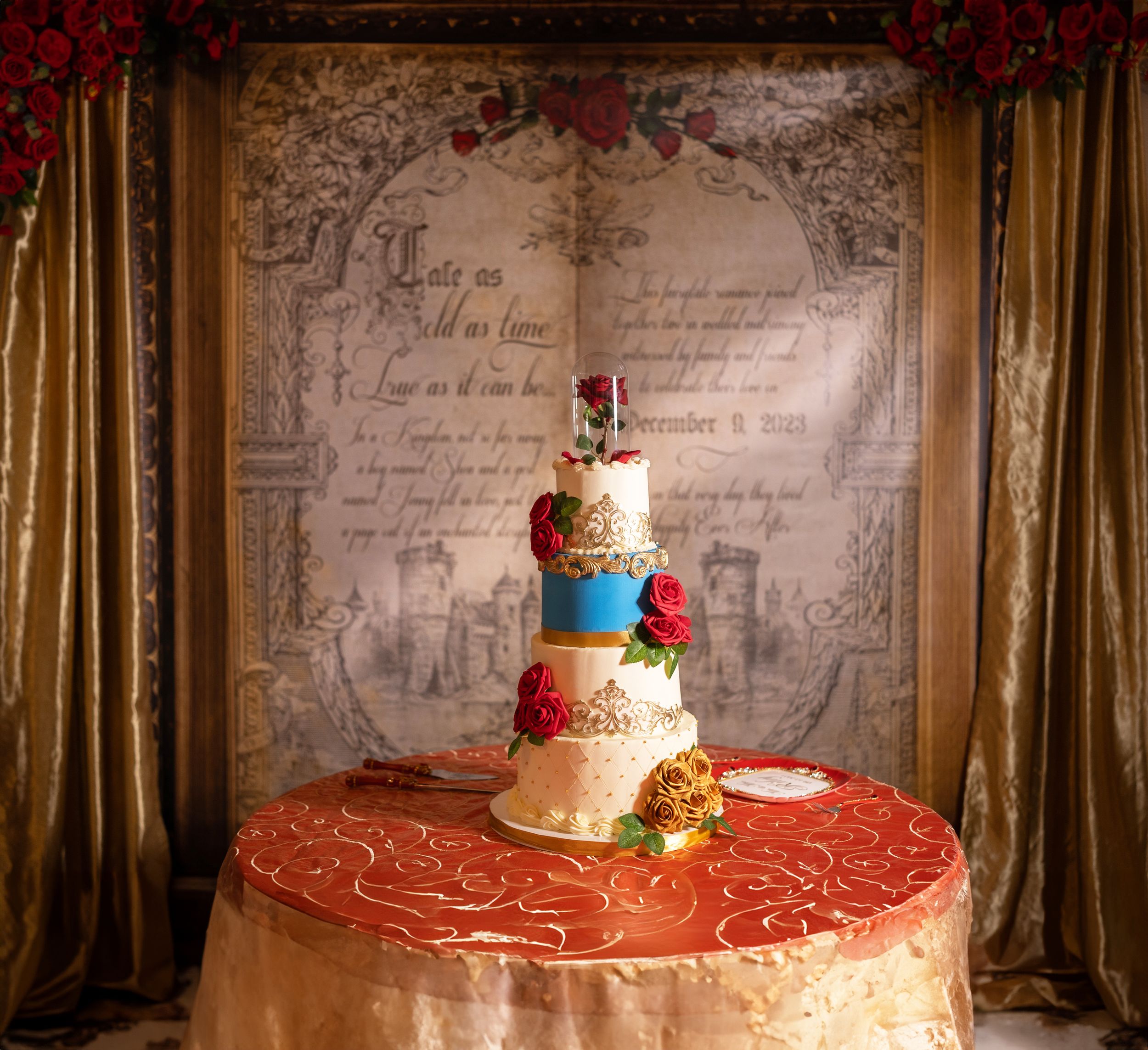 Elegant Beauty and the Beast themed wedding cake on gold table with storybook backdrop.